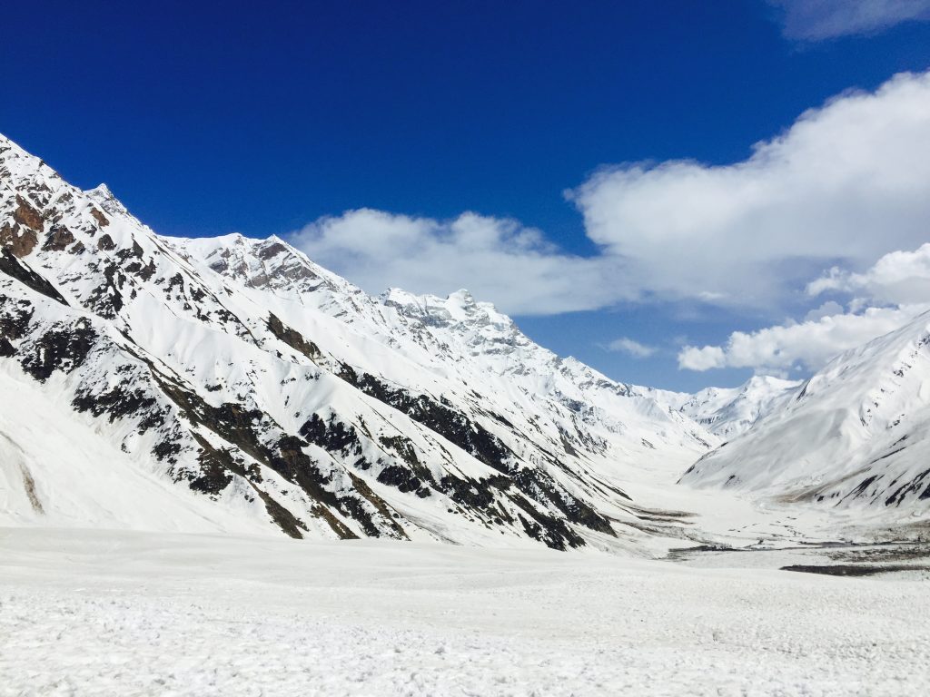 Tourists enjoying rare June snowfall at Babusar Top, playing in the snow with mountains and blue sky in the background.
