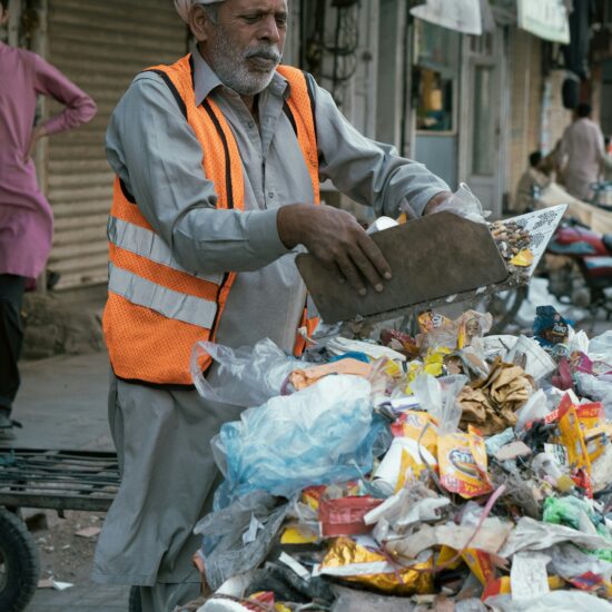 "Pakistani sanitation worker in orange vest collecting waste during Lahore Eid clean-up record operation 2025"