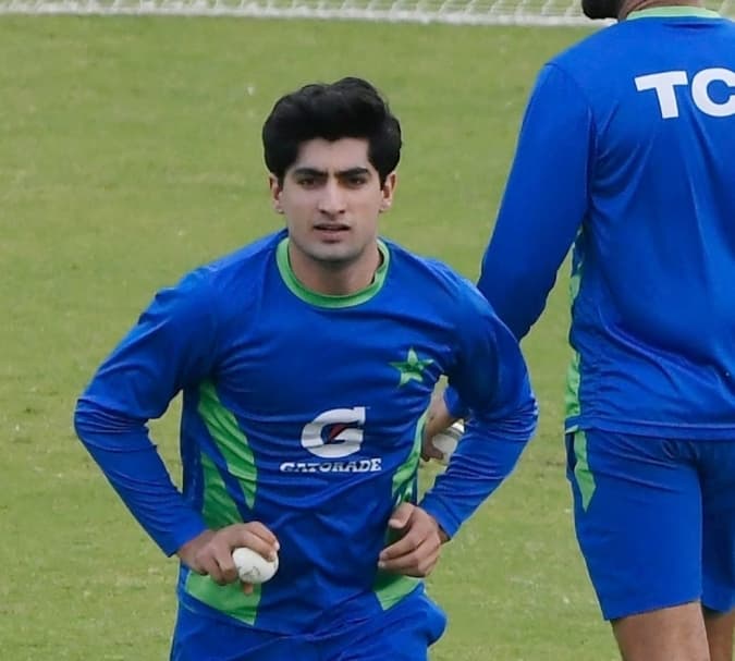 Pakistani fast bowler in action during a T20 match, delivering a fast ball with the crowd watching.
