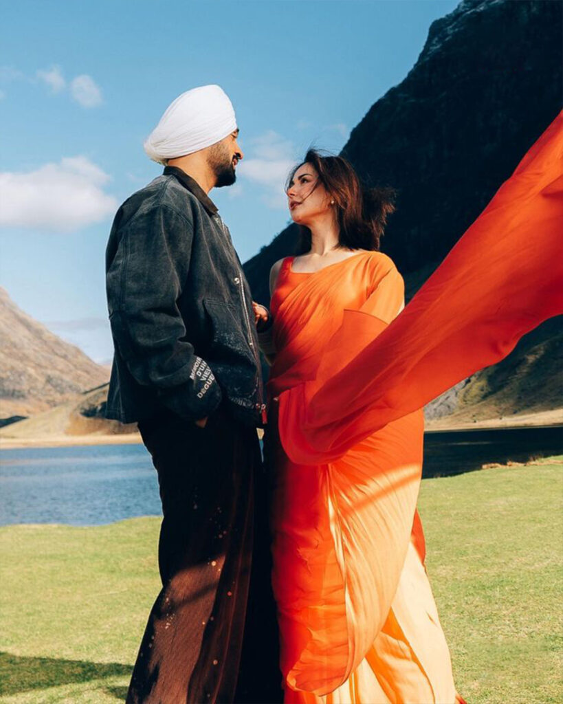 Diljit Dosanjh performing a dramatic scene in the mountains for Sardaar Ji 3, surrounded by vibrant costumes and cinematic energy.