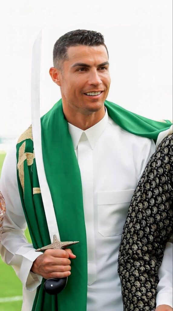 Cristiano Ronaldo in Al Nassr kit with the Saudi flag, standing before Riyadh’s skyline, surrounded by cheering fans